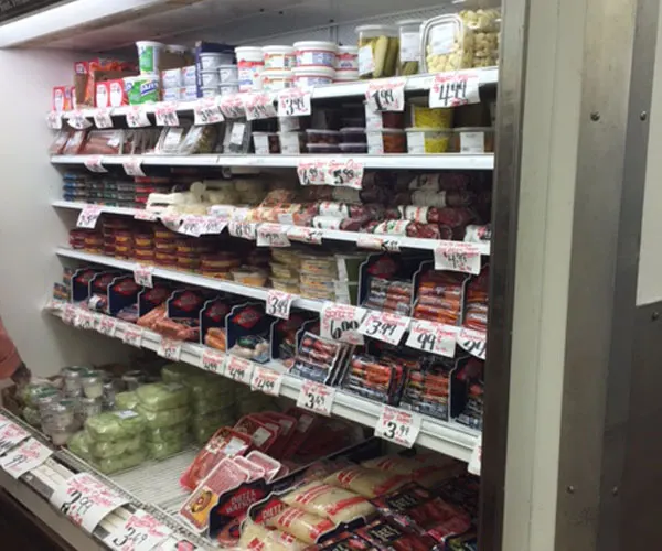 A refrigerated shelf stacked with packaged meats, cheeses and salads